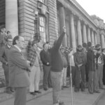 Workers from the Seamens Union and Drivers Union marched to Parliament in June 1974. They were protesting about a number of issues including cost of living and anti-union legislation being introduced that allowed injunctions on Unions supporting other unions. Pat Kelly from Wellington Trades Council (in checked jacket) with Ken Douglas (Driver Union) on his right.