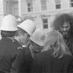 On Anzac Day in 1973 there was wreath laying by a number of countries at the Wellington Cenotaph. After the main ceremony a wreath was laid at the Wellington Cenotaph on behalf of the Victoria University Students Association. Police discuss the wreath laying with Peter Wilson. Roger Steele listens in the center facing the camera. An RSA member had objected to the VUWSA laying a wreath in the main ceremony.